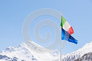 European Union and Italian flag blowing in the wind on the Alps, sunny clear blue sky