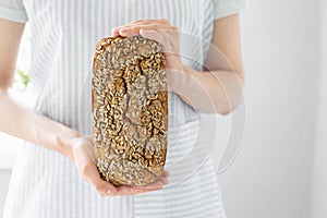 European woman baker holding buckwheat bread, white woman in a light apron holding homemade sourdough bread