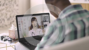 European woman gp physician, wearing coat and headset, consulting patient remotely via video call