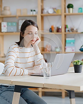 a European woman in her home office is working with a laptop or watching a webinar