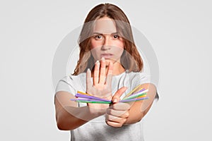 European woman with serious expression, holds plastic straws, says no to disposable plastic drinking straws in favour of metallic, photo