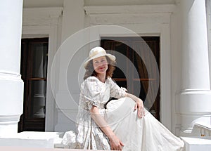 European woman sitting in sunshine and touching hair in vintage dress near palace.