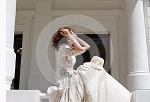 European woman sitting in sunshine and touching hair in vintage dress near palace.