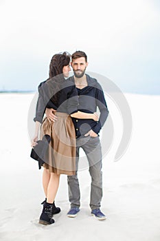 European woman wearing skirt hugging young man in monophonic winter background.