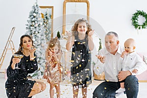 A European young family, dad, mom, son and little girls-daughters are shooting a confetti party popper at a Christmas party on