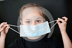 European young girl puts on a medical mask. Conceptual photo on the theme of the covid-2019 pandemic.  on a black
