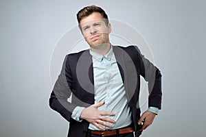 European young man in suit having stomach pain. Colic or flatulence