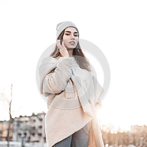 European young stylish woman fashion model in a vintage knitted hat in a fashionable faux fur coat posing at sunset. Glamorous