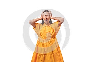 European young woman with black hair dressed in an orange summer dress screams with her ears closed and glaring