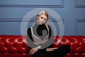 European young woman fashion model in black stylish clothes with trendy pearl hair clips in a fashionable pearl top sits on a