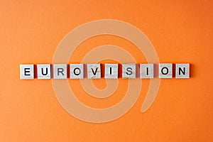 Eurovision word. The phrase is laid out in wooden letters top view. Orange flat lay background.