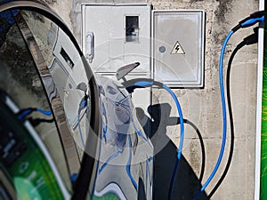 EV Car or Electric vehicle at charging station with the power cable supply plugged in on blurred nature with blue enegy