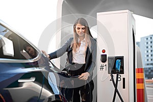 EV charging station, eco fuel concept. Portrait of pretty young girl inserting charging plug into her modern electric