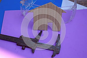 Evaluating home construction costs concept. Building shape with caliper and transparent protection glasses on purple and