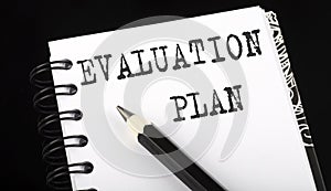 EVALUATION PLAN written text in small notebook on a black background