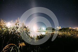 Evaporation Over River Lake Near Houses In Village. Night Starry Sky Above Misty Lake River Landscape At Night. Glowing