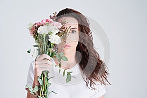 Even the flowers envy her beauty. Studio shot of a beautiful young woman holding a bouquet of flowers against a grey