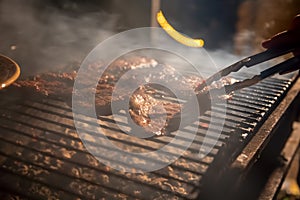 In the evening a barbecue grill on which tasty juicy steaks are grilled over an open fire, a hand holds tongs and turns