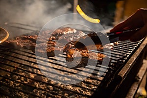 In the evening a barbecue grill on which tasty juicy steaks are grilled over an open fire, a hand holds tongs and turns