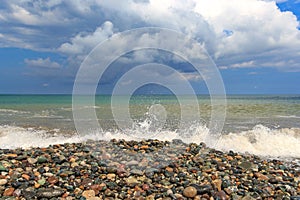 In the evening, a burst of waves on a pebble beach. Cloudy and dramatic sky before sunset. Nature concept, design for postcard.