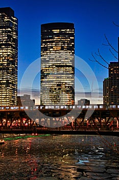 Evening in Chicago while el train travels over bridge spanning a frozen Chicago River with ice chunks.