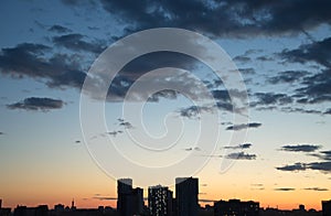 An evening city with dark buildings at sunset and dark clouds.