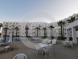 Evening in Cyprus. A swimming pool surrounded by sun loungers and parasols, tables and chairs surrounded by palm trees against a