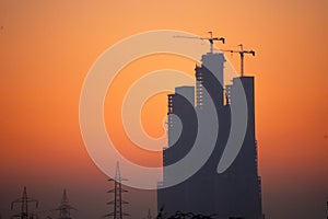 Evening dusk twilight shot showing under construction skyscraper multi story building silhouette against golden, red sky