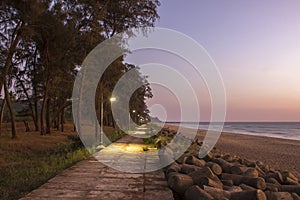 A Evening embankment with glowing lanterns on the sea coast with a sandy beach and a tsunami barrier and a green forest