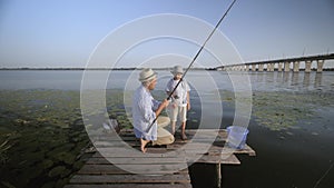 Evening fishing, dad and his happy child are together watching spinning rod for fishing while sitting on pier by the