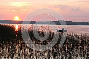 Evening fishing. Silhouette of a fisherman in a boat on the big lake. Fishing against the setting sun. Sedge growing along the