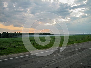 Evening fog spreads across the field along the road