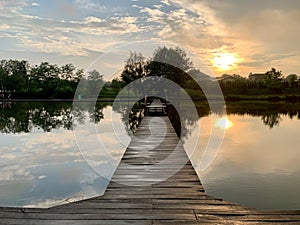 Evening landscape on a lake in the forest. Sunset on the pond. Fishing platform on the river