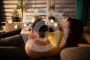 In the evening, lying on the bed, the husband kisses the belly of his pregnant wife. A woman in advanced pregnancy.