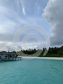 Evening in the Maldives, view of the villas in the water and the coast of the Indian Ocean with white sand and tropical trees