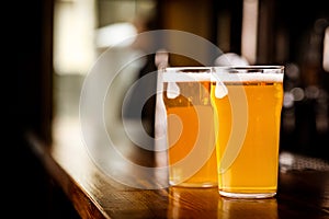Evening meeting in pub. Two glasses with light beer on wooden bar counter