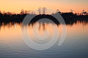 Evening mood besides a river against a containerport and sunset