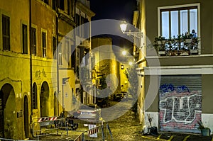 Evening narrow streets of old Rome, Italy Night with parked cars on them and glowing lanterns and houses with windows that light