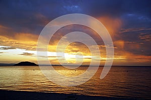 Evening over the sea. Colorful sunset. A bright red sun sets behind a mountain in the clouds. Sithonia. Greece .