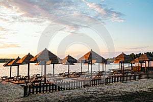 Evening sandy beach with brown wooden loungers and umbrellas