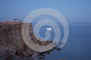 Evening sea view with cliff cape in pink light, white boat in the sea and blue horizon