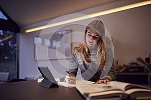 Evening Shot Of Woman In Kitchen Working Or Studying From Home Using Digital Tablet