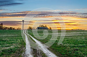 Evening sky at sunset road in the field leading to the shed barn and water tower of the rural landscape of the village.