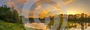 Evening spring landscape. panoramic view of the river with a hilly grassy shore against a cloudy sky with a glow from sunset