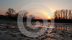 Evening spring sunset above shallow fishing pond, viewed from water surface level.