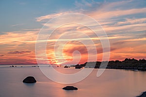 Evening sunlight on coast, pink clouds, blue sky reflection on water. Beach in summer. Seaside natural environment.