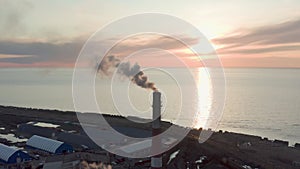 Evening sunset and blue sea Drone removes the chimney releases black smoke. The coal processing factory pollutes the