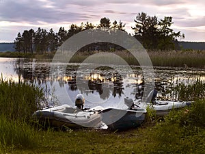Evening sunset on the lake. Three boats on the shore. The sun sets and is reflected in the water.