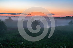 Evening thick fog over field and forest. Landscape of the evening sky with fog, orange and blue sky.