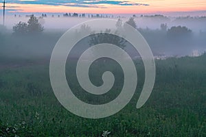 Evening thick fog over field and forest. Landscape of the evening sky with orange and blue sky and fog.